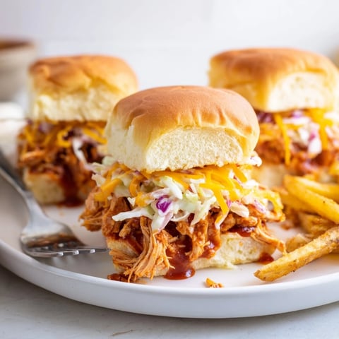 Juicy BBQ Chicken Sliders stacked on soft buns, served alongside crispy golden fries.  