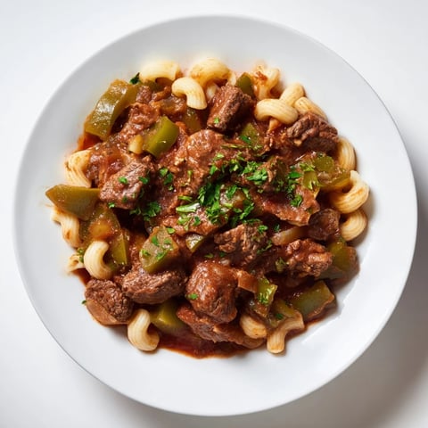 Steaming bowl of goulash with beef and pasta, garnished with fresh parsley, ready to enjoy.