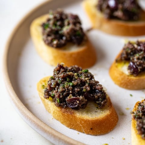 Golden toasted crostini topped with vibrant black olive tapenade, ready to enjoy at any gathering.