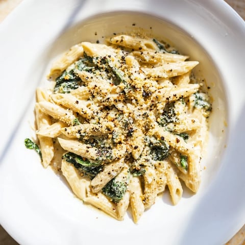 Steaming Creamy Spinach Pasta, creamy sauce engulfs penne, inviting with garlic and fresh spinach.