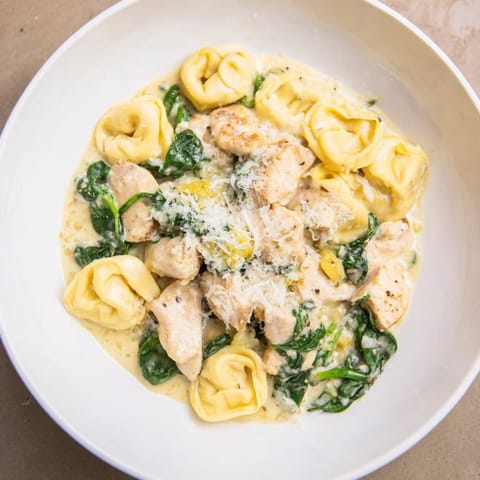 Enjoy a bowl of warm Creamy Chicken and Spinach Tortellini, garnished with fresh parsley and extra cheese.