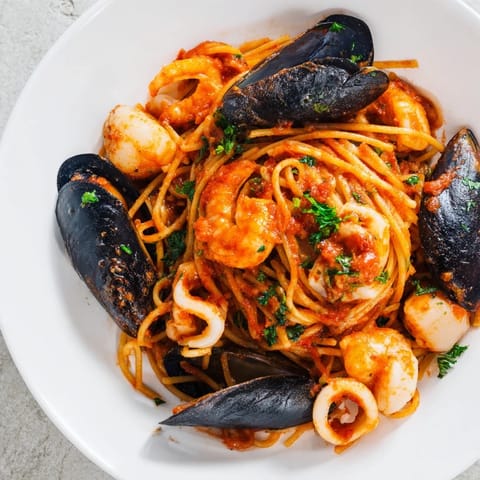 A steaming bowl of Seafood Marinara Pasta, garnished with parsley and lemon wedges looks tempting.