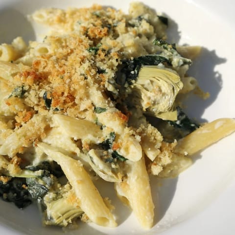 Close-up of creamy Artichoke Pasta Bake with tender pasta, wilted spinach, and marinated artichoke hearts in a rich sauce.